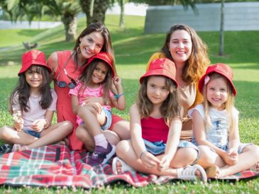 Friends enjoying a sunny day picnic on grass with bucket hats and smiles in a Portuguese park.