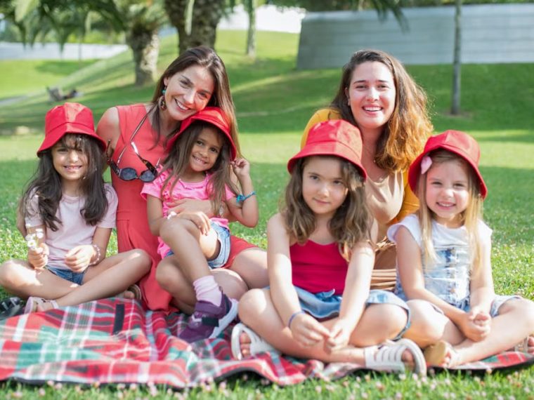 Friends enjoying a sunny day picnic on grass with bucket hats and smiles in a Portuguese park.